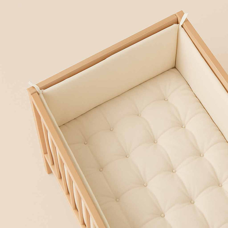 Natural wool crib bumper and tufted crib mattress inside wooden crib