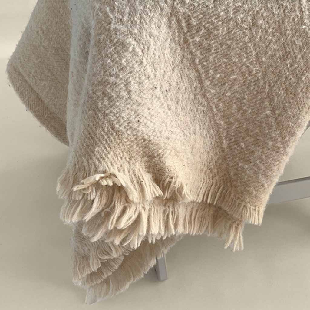 Textured wool blanket with soft fringed edges, draped over a chair, offering natural warmth and breathable comfort