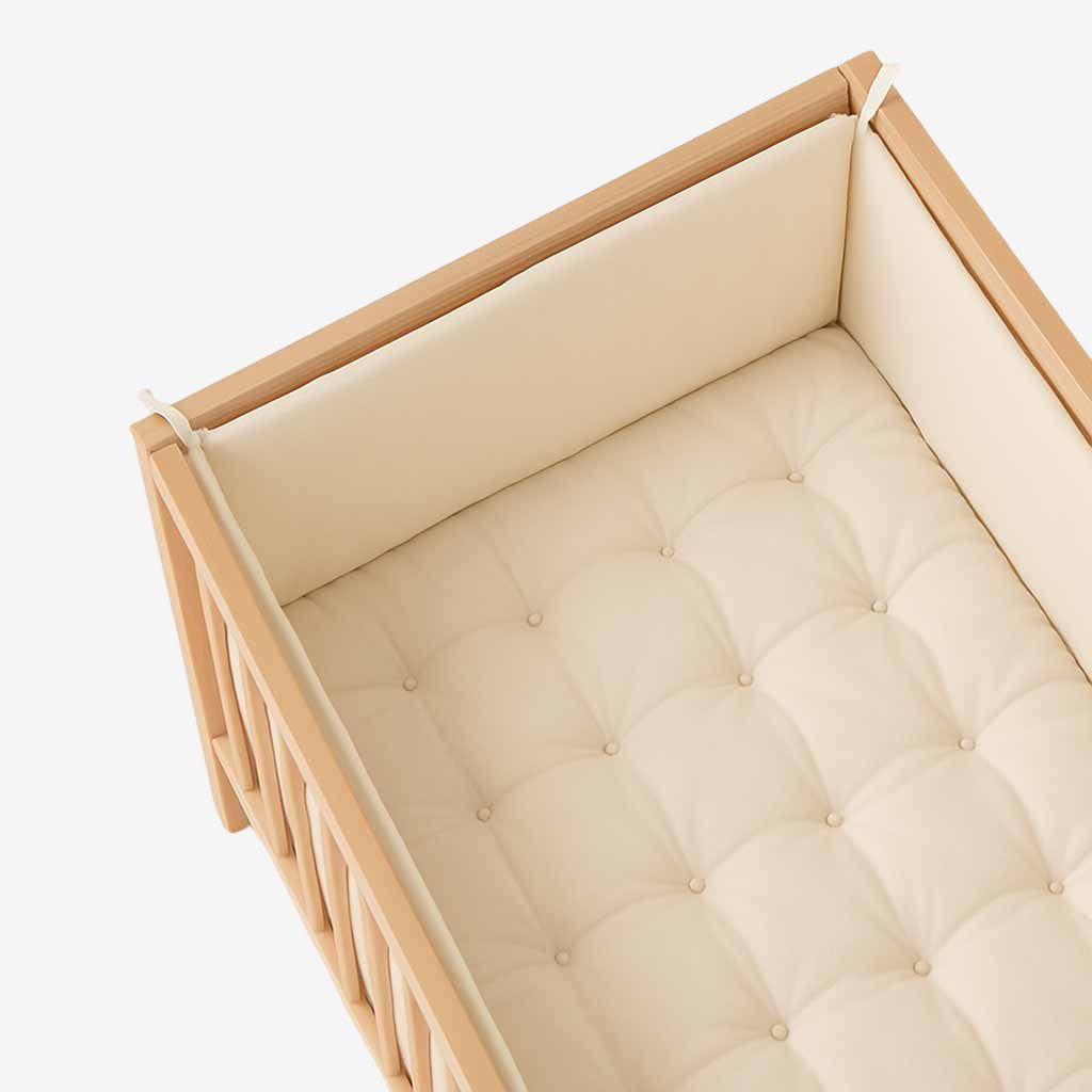 Natural wool crib bumper and tufted crib mattress inside wooden crib.
