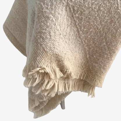 Textured wool blanket with soft fringed edges, draped over a chair, offering natural warmth and breathable comfort.