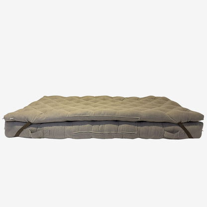 Brown linen wool mattress topper layered on wool mattress – side view showing straps, tufting, and zipper.